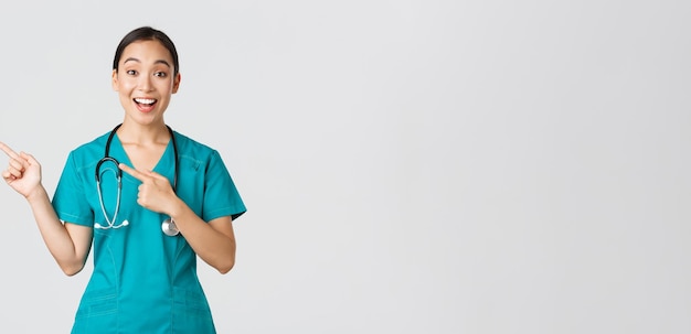 Free photo covid healthcare workers pandemic concept excited asian nurse doctor in scrubs and stethoscope point...