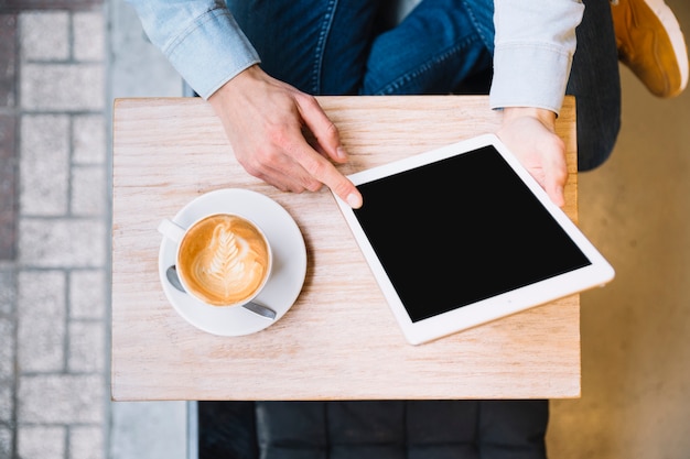 Free photo crop hands holding tablet with coffee nearby