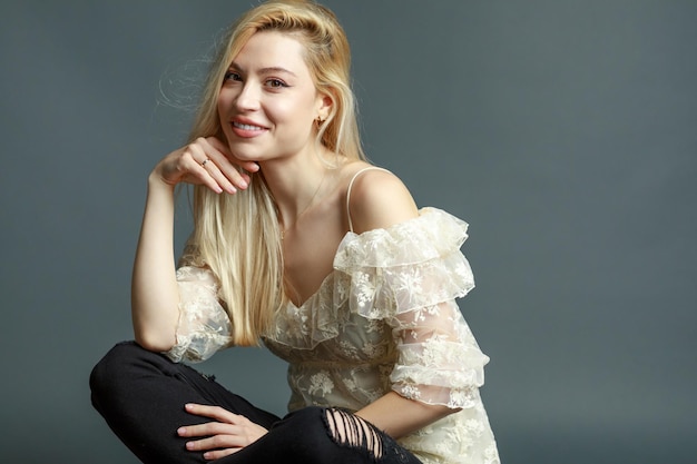 Free photo cute blonde sitting on grey background and smiling to the camera