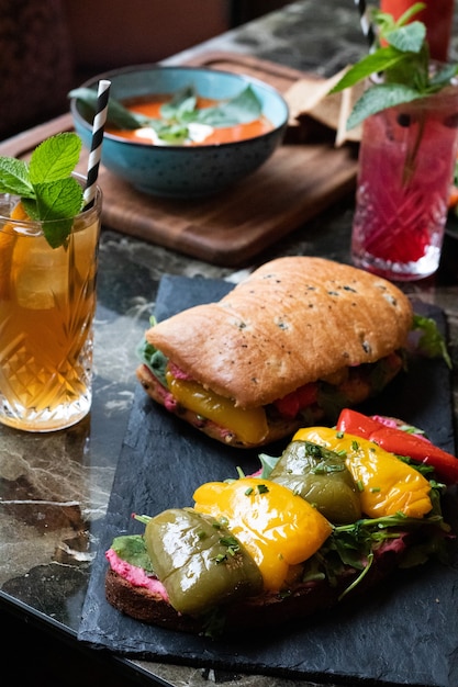 Free photo delicious sandwich with sauce, greens, roasted bell peppers and glasses of fresh juice with straws