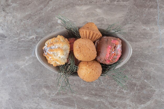 Dessert assortment on a small bowl adorned with pine leaves on marble surface