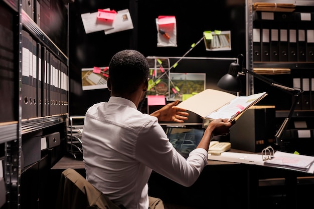 Free photo detective looking at evidence on board and comparing with police report. investigator holding folder with forensic expertise, analyzing clues and photos attached to office wall