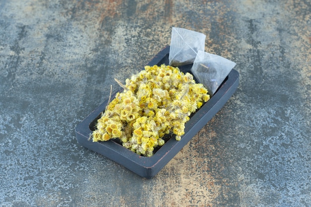 Free photo dried chrysanthemum and teabags on dark plate.