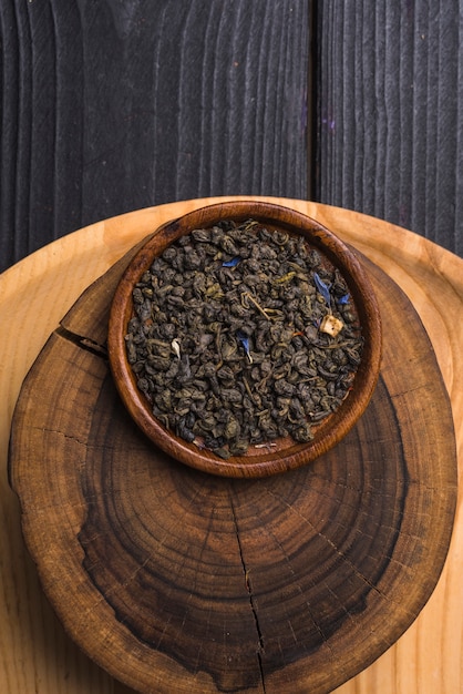 Free photo dried tea leaves on wooden plate over the tree stump against table