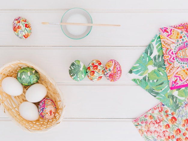 Free Photo easter eggs in basket near napkins and brush on cup with dye liquid