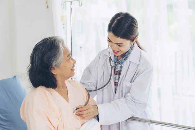 Free photo elderly female smiling with doctor and visiting senior patient woman at hospital ward