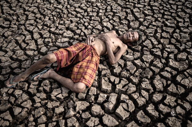 Free photo elderly men lay flat, hands placed on the belly on dry and cracked soil, global warming