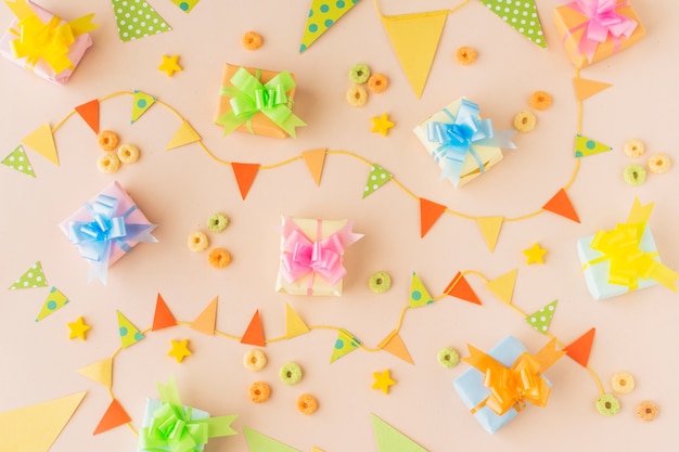 Free photo elevated view of birthday gifts; bunting and froot loops candies on colored background