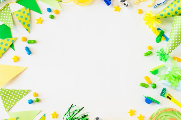 Free photo elevated view of bunting; candies; party horn blower; whistle and hat on white surface