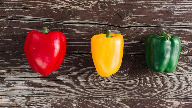 An elevated view of red; yellow and green bell peppers on damaged wooden surface