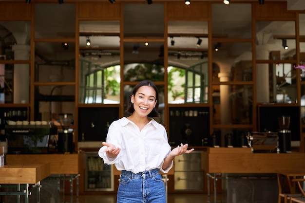 Foto gratuita entusiasta giovane imprenditrice ragazza asiatica che mostra la sua attività alzando le mani e sorridente standi