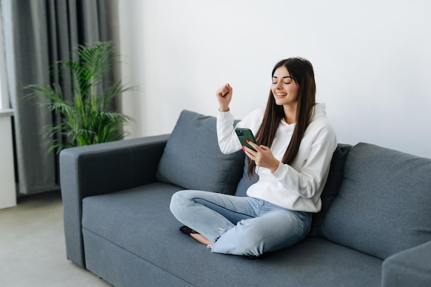 Free photo excited woman watching media content on line in a mobile phone sitting on a couch in the living room at home