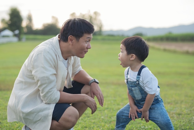 무료 Photo 아버지와 아들이 일몰 시간에 공원에서 연주. 사람들은 현장에서 재미. 친절한 가족과 여름 휴가의 개념. 아버지와 아들 다리 공원에서 잔디밭을 가로 질러 걸어