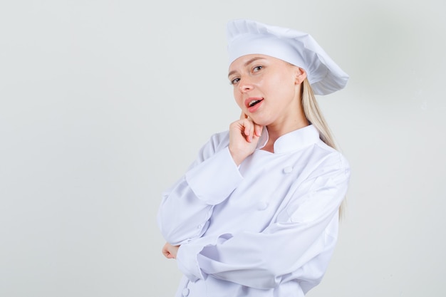 Foto gratuita cuoco unico femminile che tiene il dito sulla guancia in uniforme bianca e dall'aspetto affascinante.