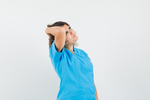 Free photo female doctor in blue uniform looking up with hand on hair and looking elegant