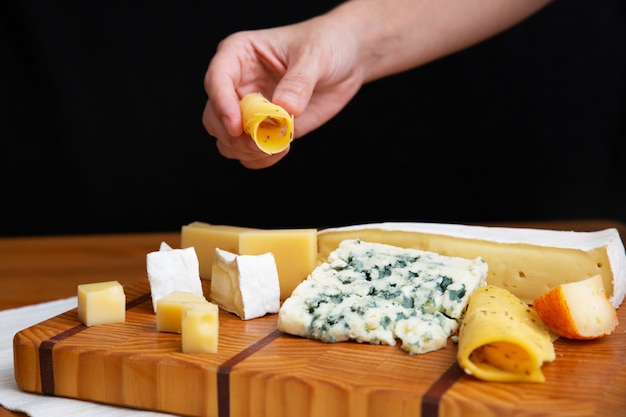 Free photo female hand taking slice of cheese from wooden board