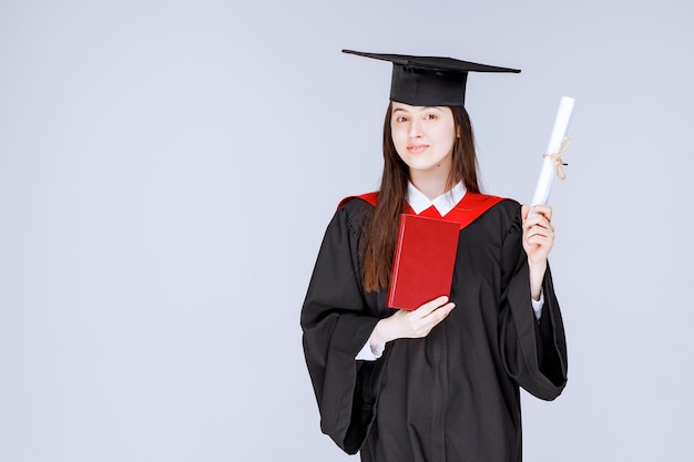 Female student in academic gown holding book and diploma. High quality photo