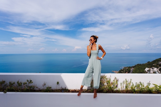 Free Photo fit tanned caucasian woman in light blue mint color overall on teracce balcony of luxury villa with amazing tropical sea view