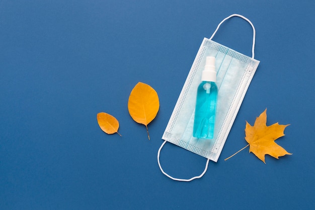 Free photo flat lay of medical mask with hand sanitizer and autumn leaves