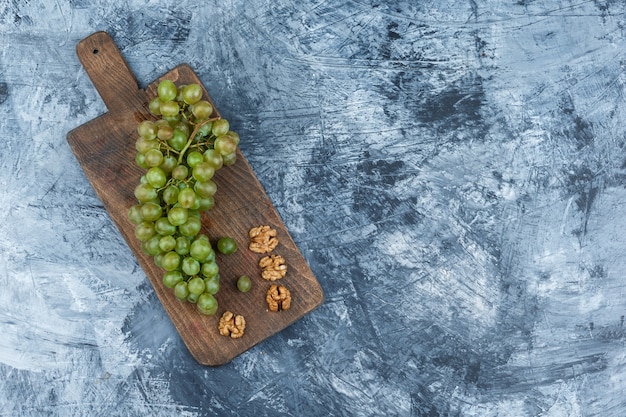 Free photo flat lay white grapes, walnuts on cutting board on dark blue marble background. horizontal free space for your text