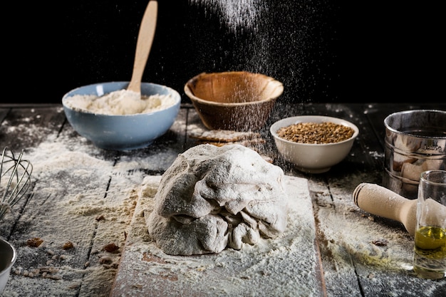 Foto gratuita farina che cade sulla tavola da forno con gli ingredienti nella ciotola