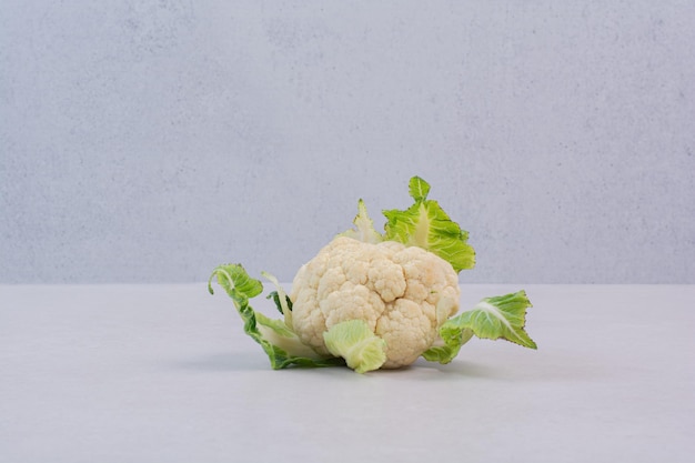 Foto gratuita cavolfiore fresco con foglie sul tavolo bianco.