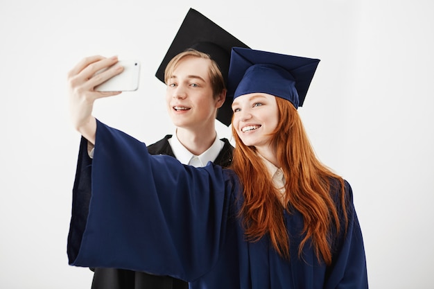 Free photo friends graduates of college in caps smiling making selfie.