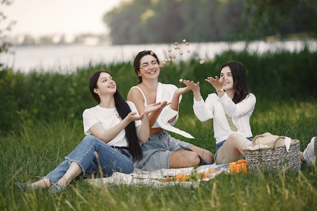 Friends sitting on a grass. Girls on a blanket. Woman in a white shirt.