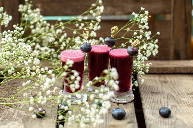 A front close up view fresh cocktails around flowers and on the brown wooden surface