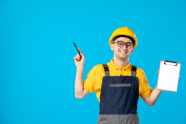 Free Photo front view of cheerful male builder in uniform with file note in his hands on blue wall