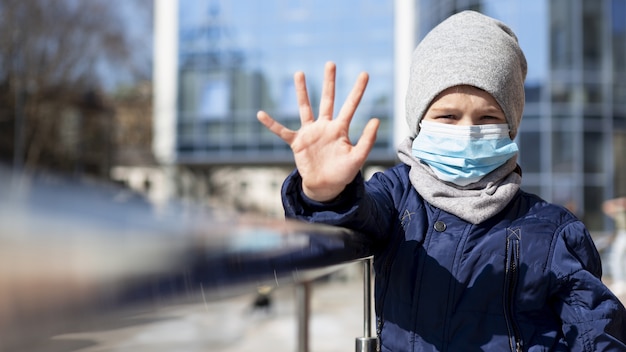 Free photo front view of child showing hand while wearing medical mask outside