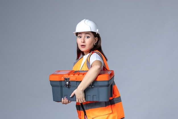 Free photo front view of female builder holding tool case on gray wall