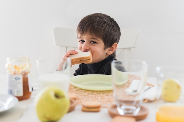 Foto gratuita bambino di vista frontale che mangia panino alla tavola