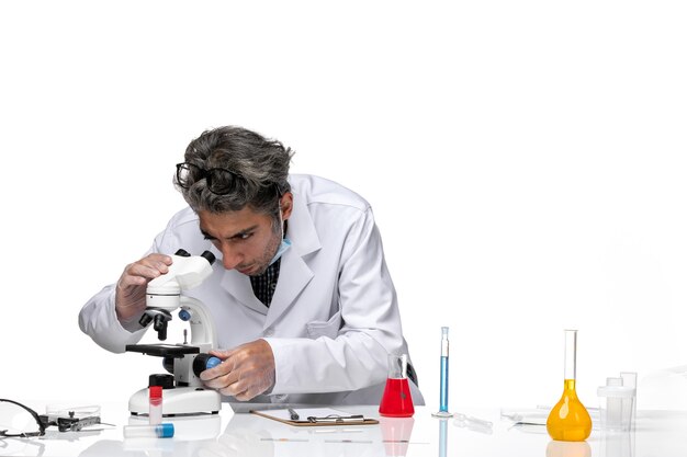 Free photo front view middle-aged scientist in special white suit using microscope