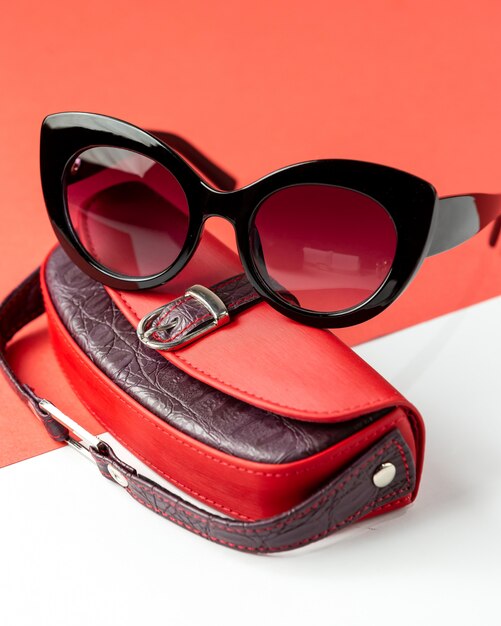 A front view modern dark sunglasses along with red leather bag on the white-red