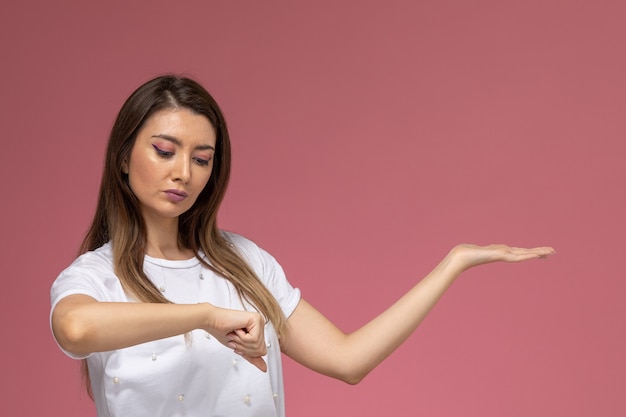 Free photo front view young female in white shirt posing looking at her wrist on the pink wall, color woman pose model woman