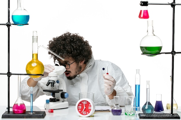 Free photo front view young male scientist in special suit holding samples and using microscope on white wall