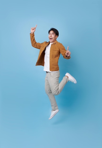 Free Photo full length asian man jumping with hand pointing finger isolated on blue copy space background