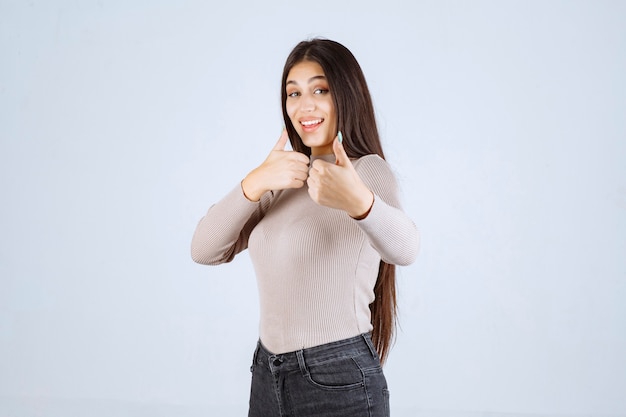 Foto gratuita ragazza in camicia grigia che fa il pollice sul segno.