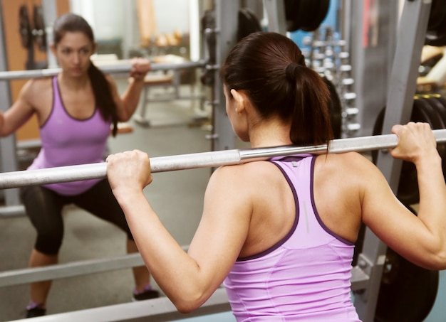 Free photo girl in the gym lifts the bar in front of the mirror