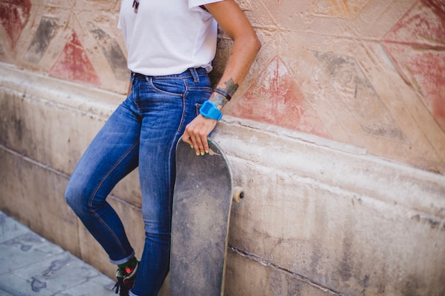 Foto gratuita ragazza che tiene skateboard appoggiato al muro di cemento