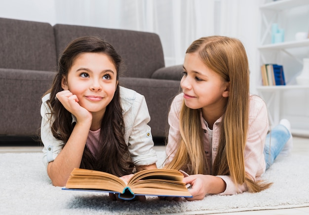 Free photo girl looking at her thoughtful friend while reading book in the living room