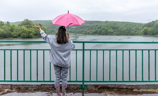 Free photo a girl walks under an umbrella in rainy weather on a bridge in the forest.