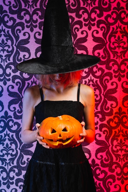 Free photo girl in witch hat holding pumpkin