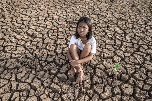 Free photo girls sitting hugging their knees, looking at the sky and having trees on dry ground