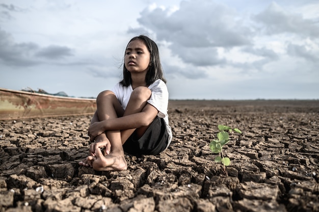 Free photo girls sitting hugging their knees, looking at the sky and having trees on dry ground