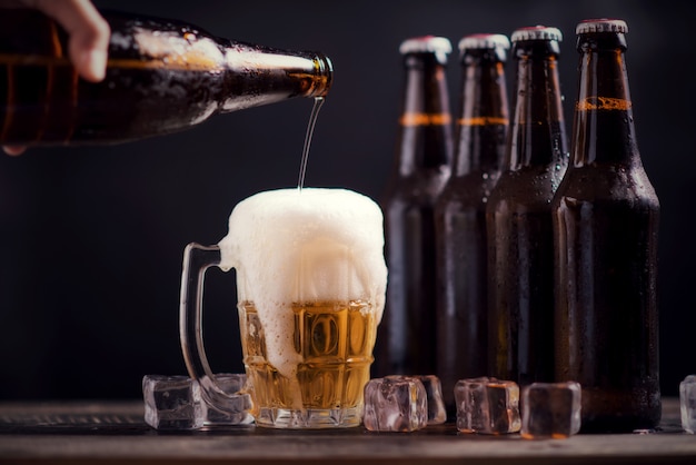 Free photo glass bottles of beer with glass and ice on dark background