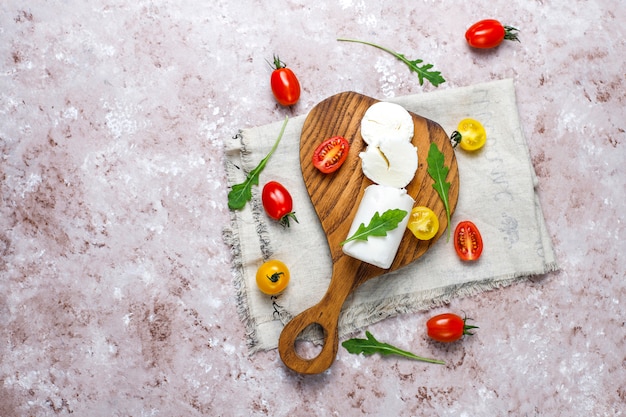 Free photo goat cheese slices on wooden board with ruccola,cherry tomatoes. ready to eat.