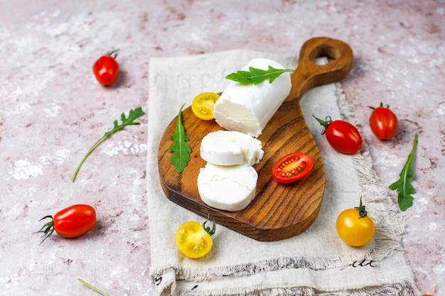 Free photo goat cheese slices on wooden board with ruccola,cherry tomatoes. ready to eat.