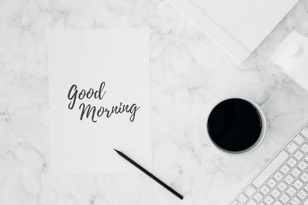 Free photo good morning written on white paper with pencil; coffee cup; diary; milk carton and keyboard on textured desk